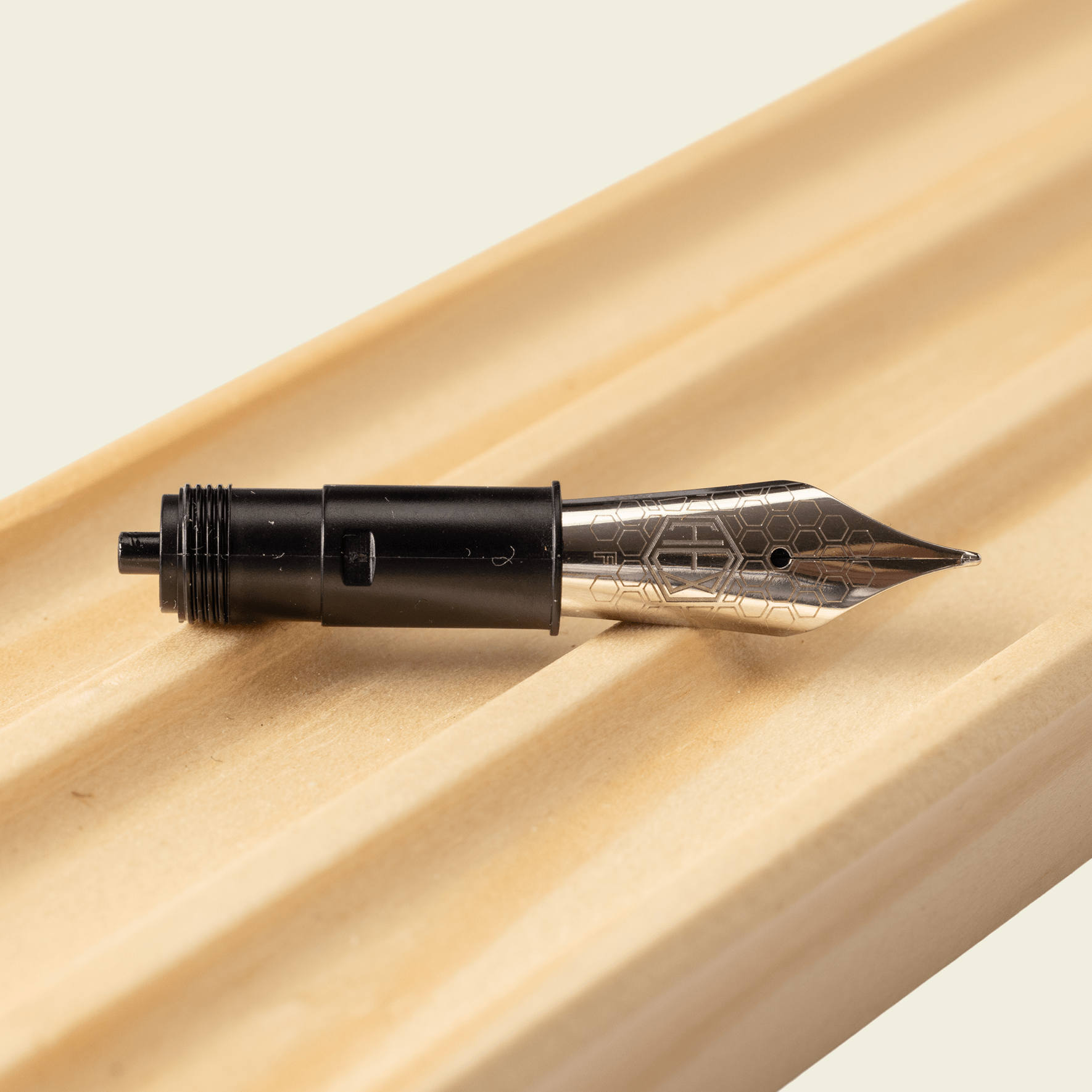 Hex Pens nib unit displayed on a wooden surface with round grooves, by Hex Pens.