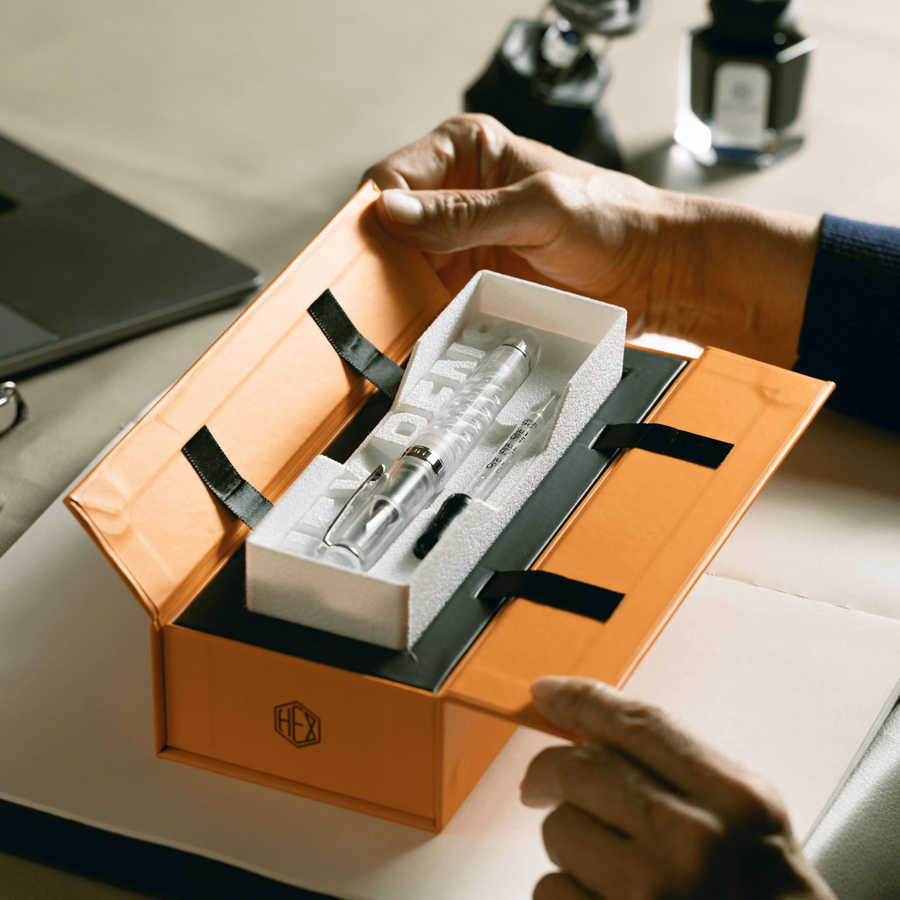 Uninked Triple Twist Lucent fountain pen with an eyedropper inside the box, both hands in the process of opening it, by Hex Pens.